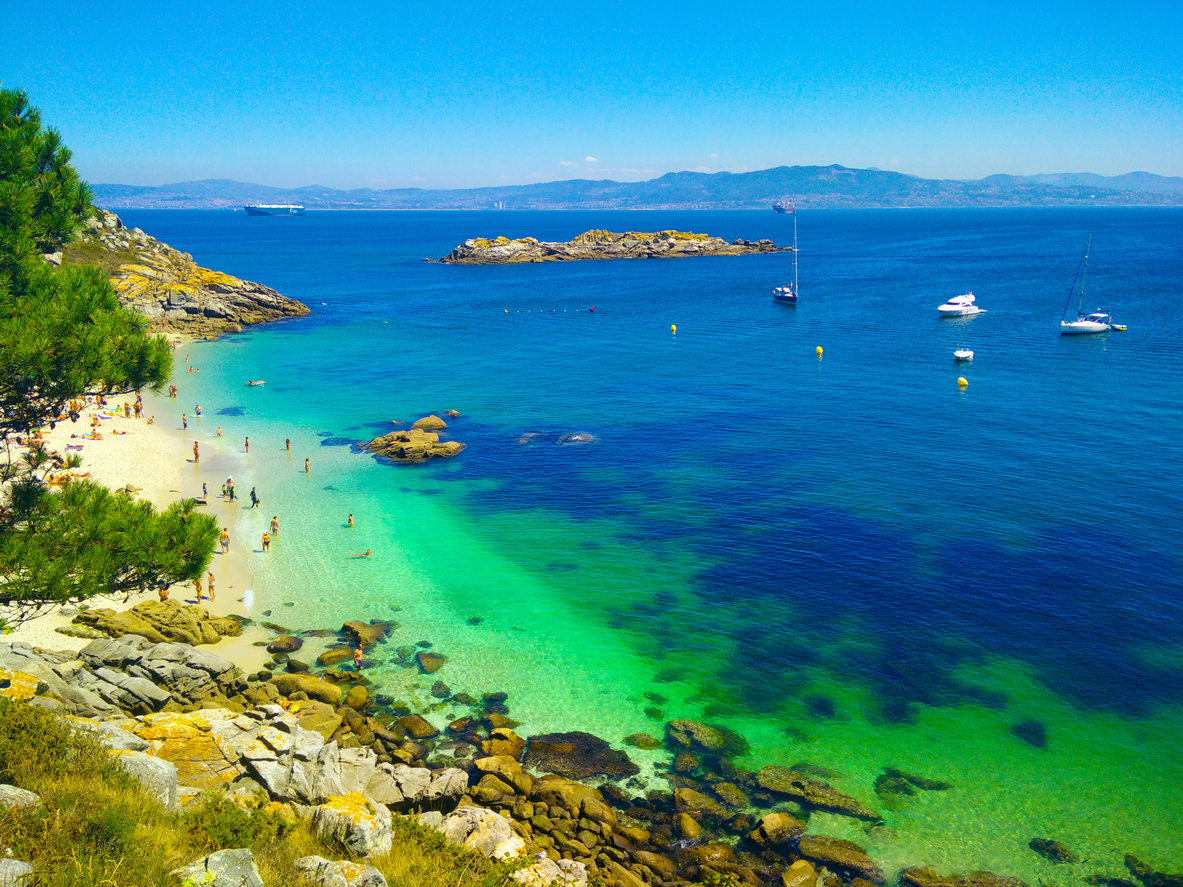Beach with transparent green water in Cies Islands, in Galicia, Spain, with boats docked in front of